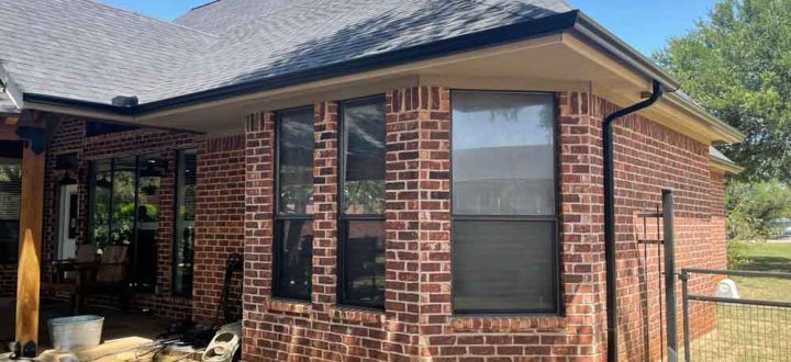 A brick home with black seamless gutters, downspouts, and dark-framed windows installed by Lone Star Seamless Gutters